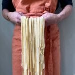 Fresh homemade pasta dough held in hands with orange apron
