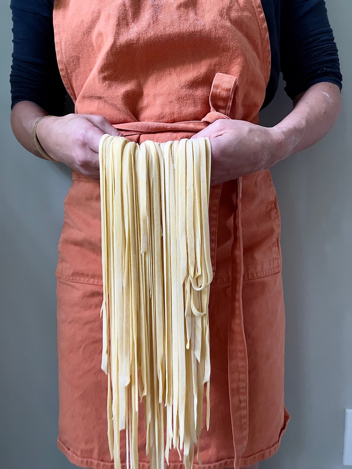 Fresh homemade pasta dough held in hands with orange apron
