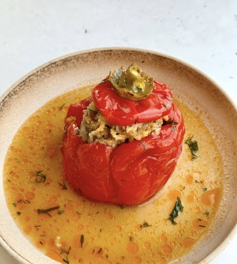 Red bell pepper stuffed with rice and meat in a tomato broth, served on a beige plate.