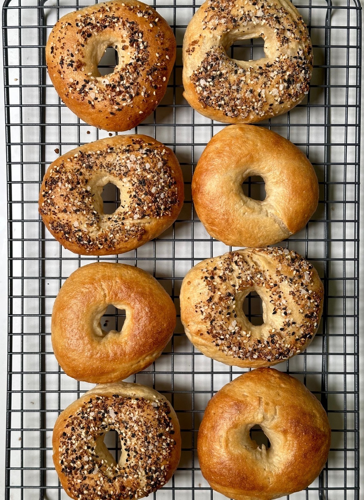 Freshly baked sourdough bagels cooling on a wire rack, some topped with everything seasoning.
