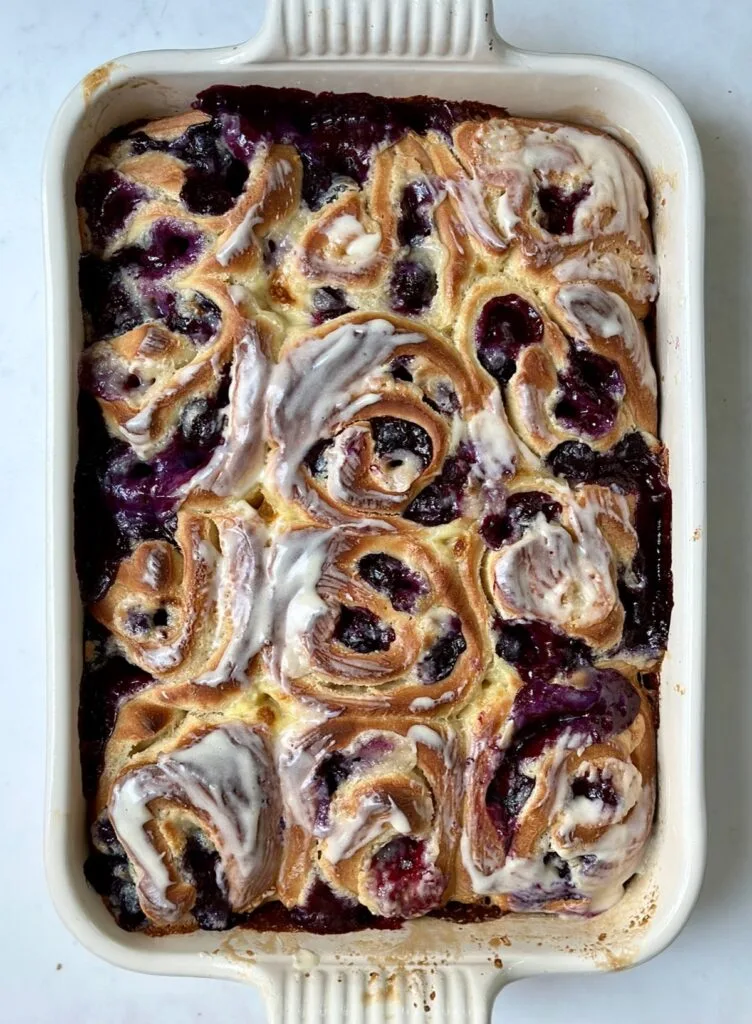 Homemade blueberry cream cheese rolls baked in a dish with icing glaze
