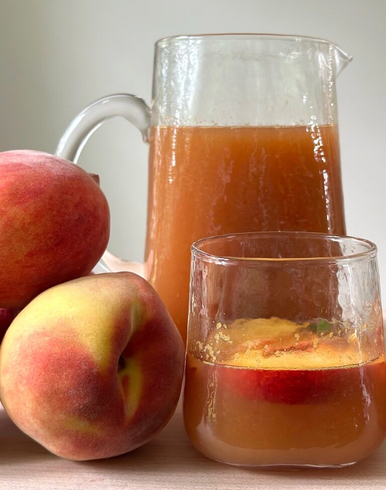 Glass pitcher and glass of peach iced tea with fresh peaches on the side. Homemade iced tea made with real peaches and honey.