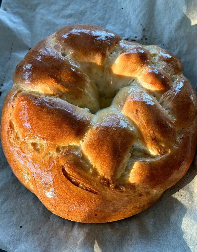Golden round braided bread with shiny crust on parchment.