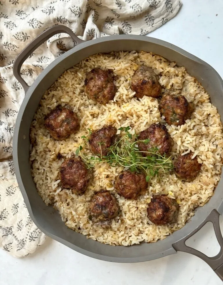 One-pot baked meatballs with rice in a skillet, garnished with fresh herbs.