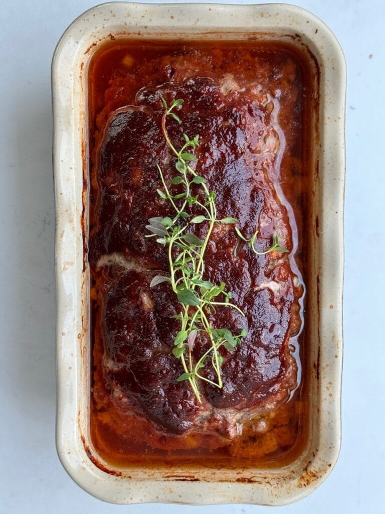 Homemade meatloaf baked in a loaf pan, topped with a rich tomato glaze and fresh thyme.