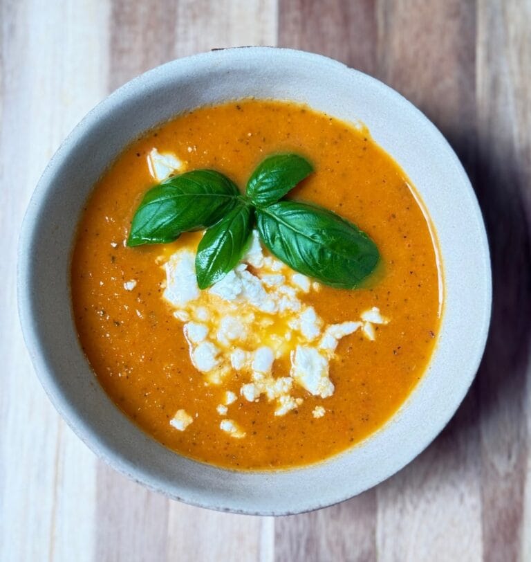 Creamy roasted vegetable soup topped with feta and fresh basil in a white bowl.