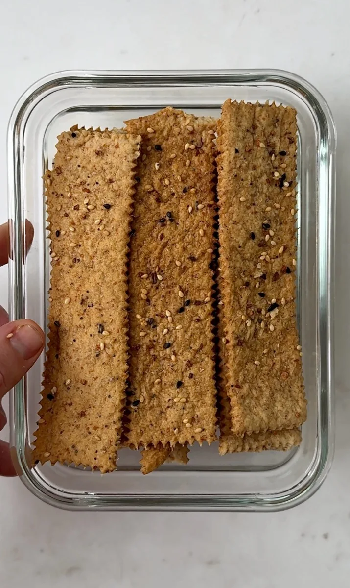 Crispy homemade sourdough discard crackers with sesame seeds in a glass container.