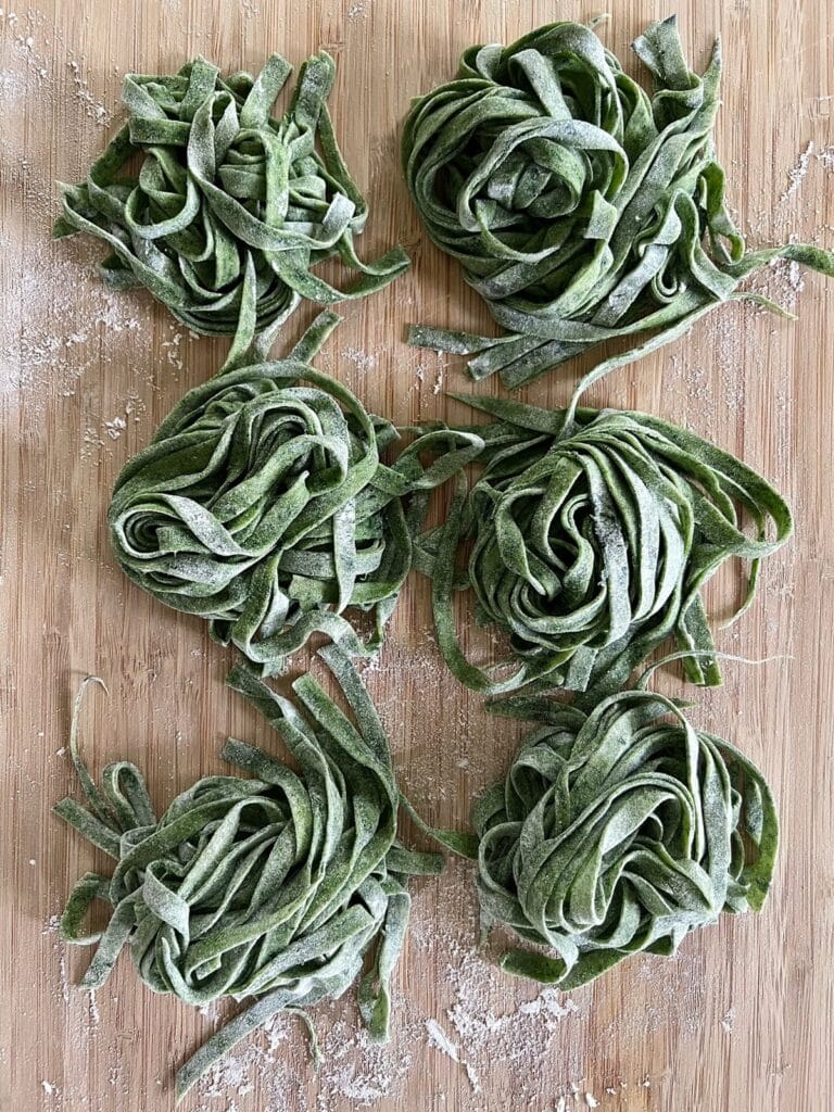 Homemade spinach pasta nests dusted with flour on a wooden board.