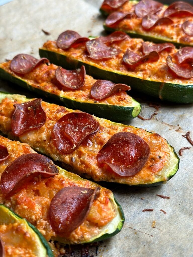 Zucchini pizza boats topped with melted cheese and crispy pepperoni slices on a baking tray.
