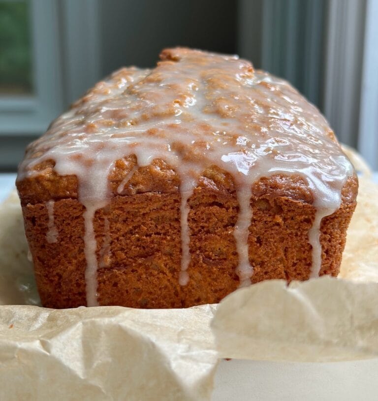 Glazed cinnamon apple bread loaf with icing dripping down the sides.