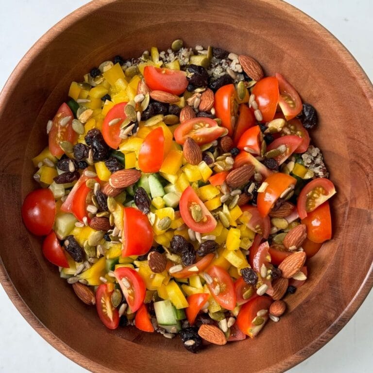 Fall quinoa salad with cherry tomatoes, yellow bell pepper, cucumber, dried berries, almonds, and seeds in a wooden bowl.