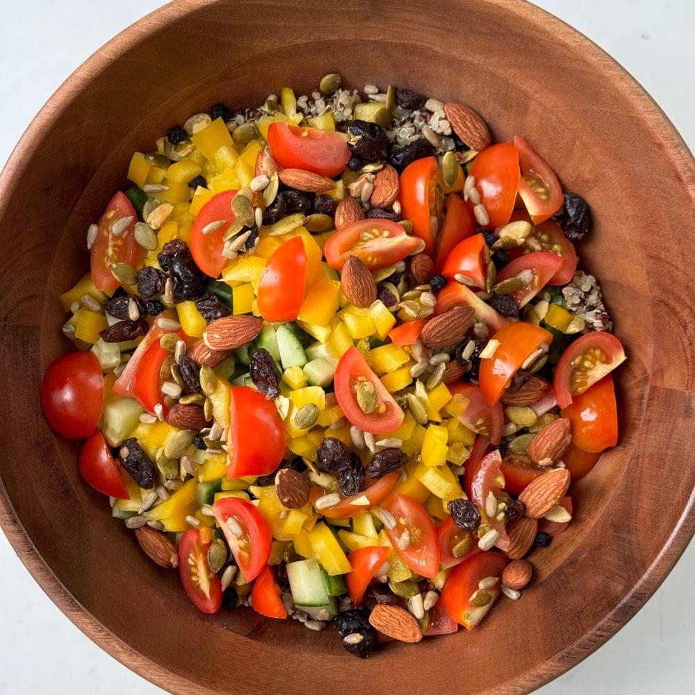 Fall quinoa salad with cherry tomatoes, yellow bell pepper, cucumber, dried berries, almonds, and seeds in a wooden bowl.
