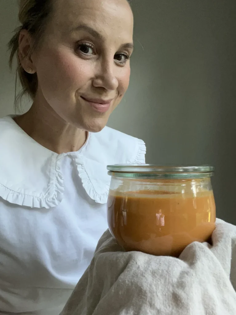 Marina smiling while holding a glass jar of homemade soup wrapped in a linen towel